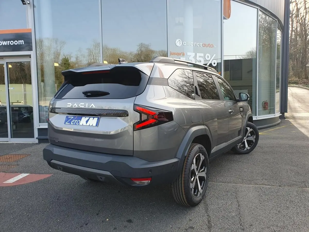 Vue 3/4 arrière droite du Dacia Bigster gris schiste avec jantes alliage 18 pouces et barres de toit longitudinales.