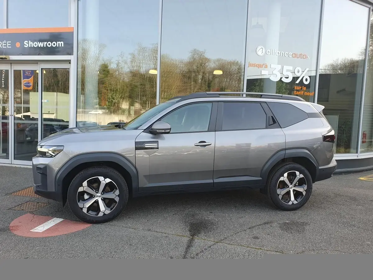 Vue de profil côté gauche d’un Dacia Bigster gris schiste avec jantes alliage 18” diamantées, toit panoramique et barres de toit.