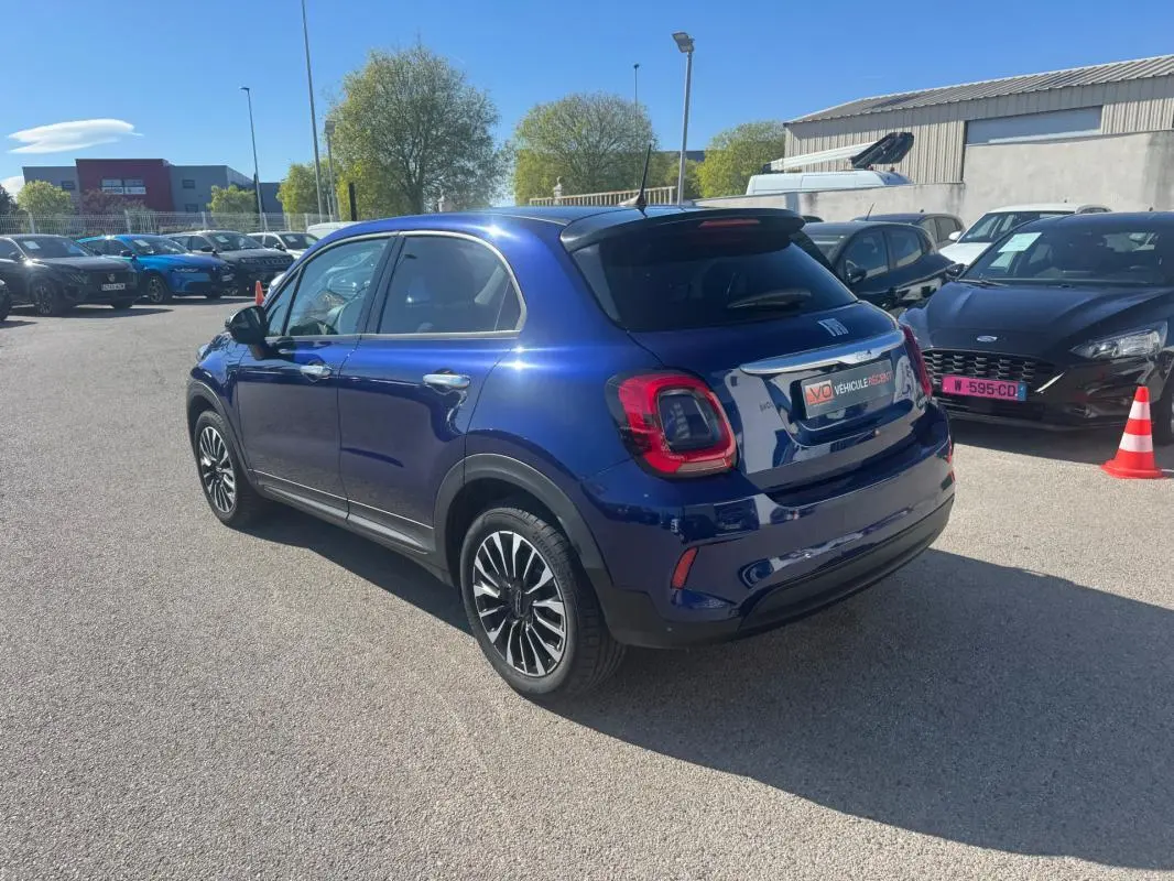 Vue 3/4 arrière droite d'une FIAT 500X bleu métallisé avec jantes classiques 16 pouces, stationnée en extérieur.