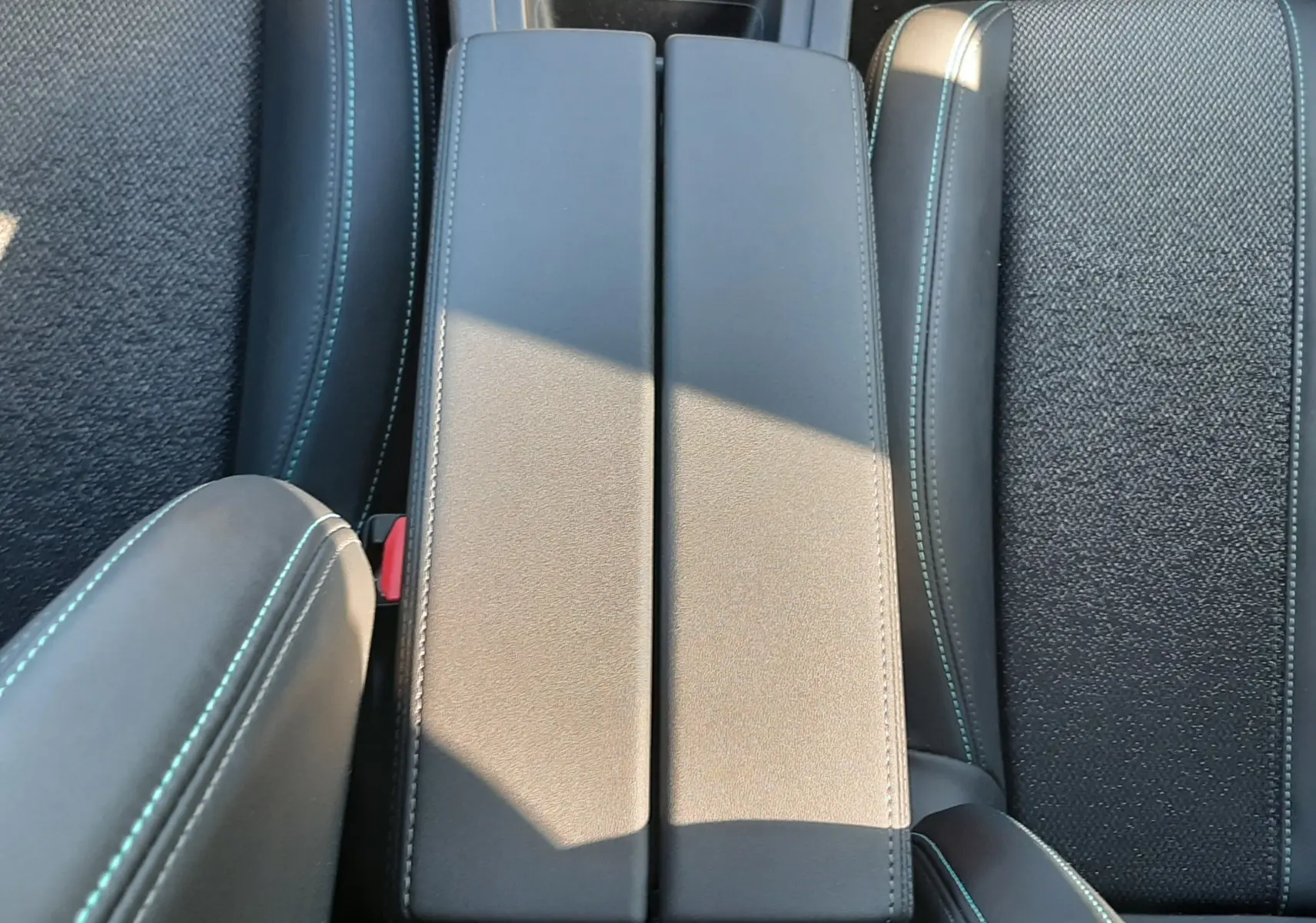 Vue plongeante sur l'accoudoir central en cuir gris avec surpiqûres bleues, entouré de sièges tissu gris du Peugeot 308 SW Hybrid 2025.