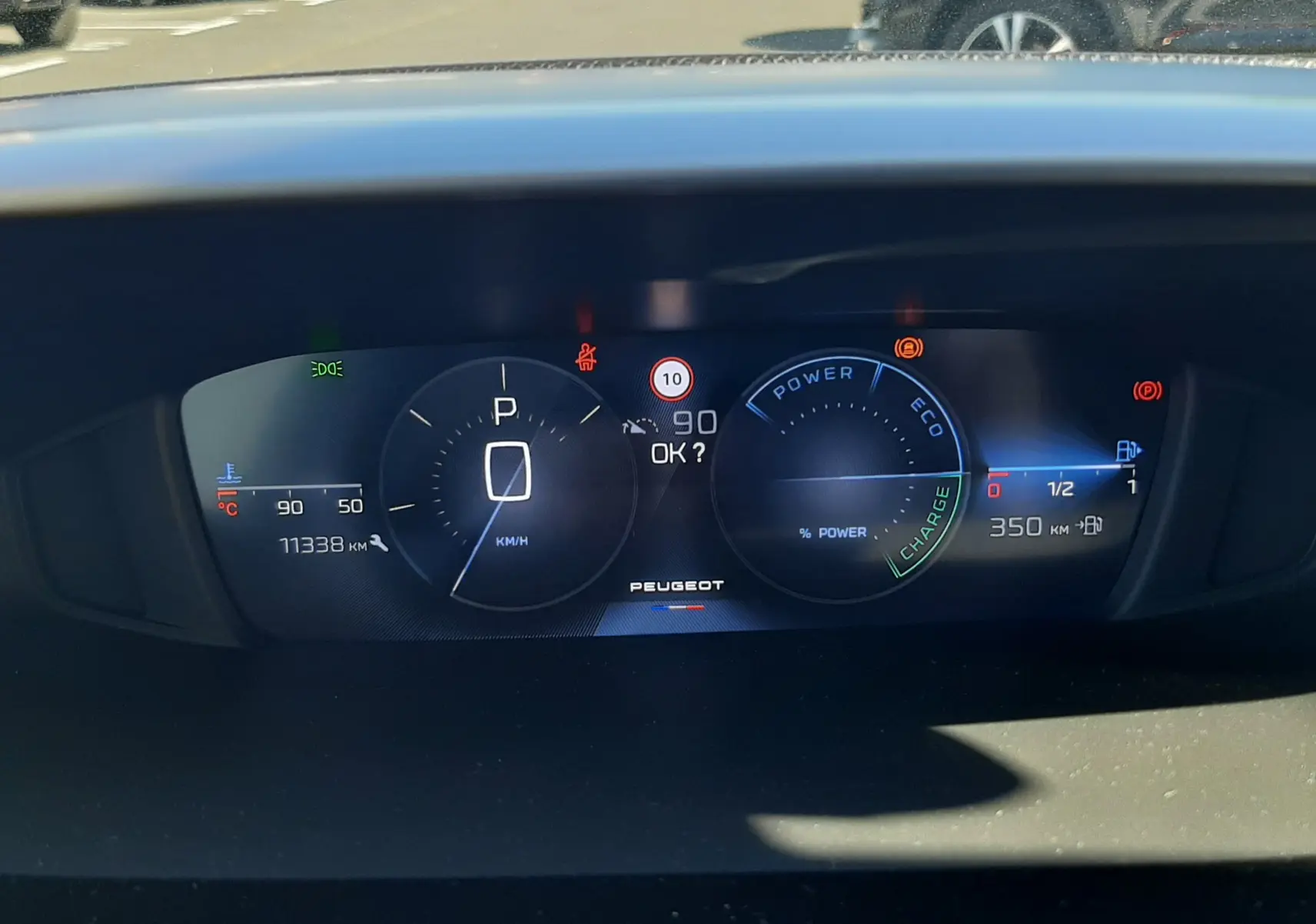 Vue rapprochée du tableau de bord numérique de la Peugeot 308 SW Hybrid, affichant la vitesse à 0 km/h et l'autonomie restante.