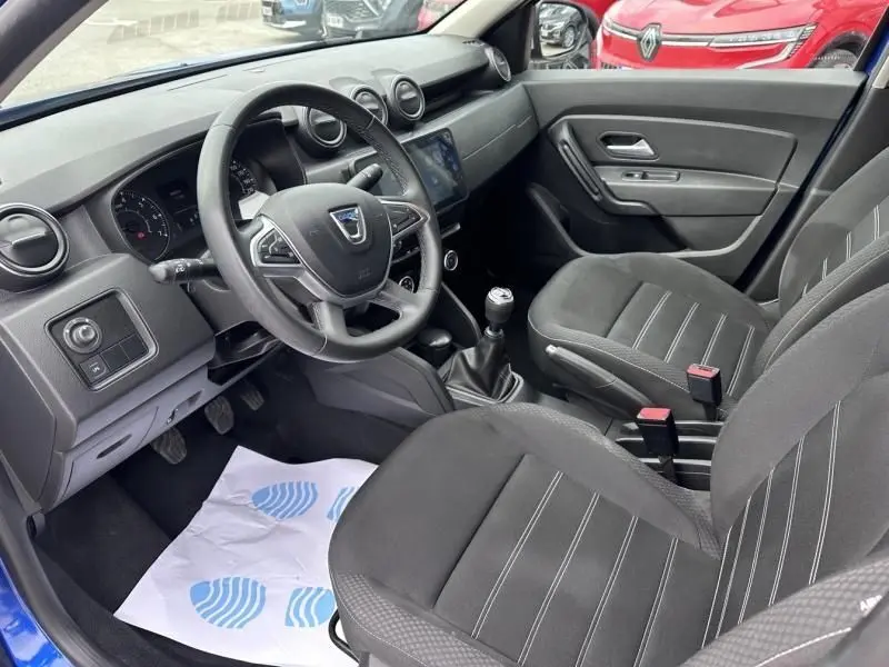 Vue intérieure côté conducteur du Dacia Duster bleu métal 2022, avec volant, tableau de bord et sièges en tissu noir.