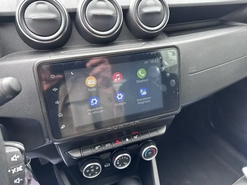 Vue rapprochée de la console centrale du Dacia Duster 2022, écran tactile avec commandes climatisation et aérateurs ronds.