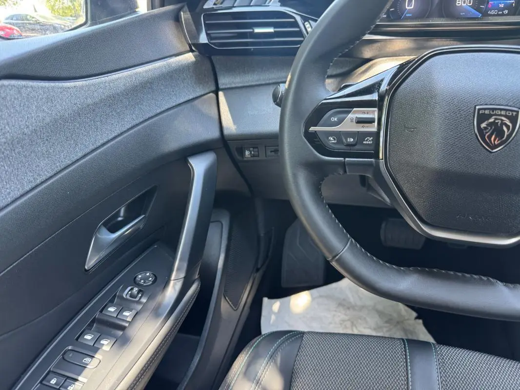 Vue intérieure côté conducteur de la Peugeot 308 gris, avec volant multifonction et commandes des vitres électriques.