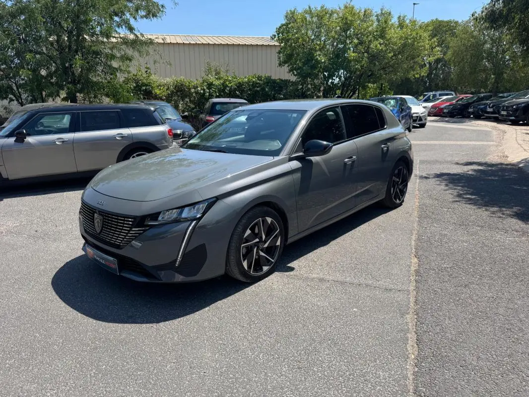PEUGEOT 308 gris en 3/4 avant droit, avec jantes alliage noires et calandre distinctive moderne.