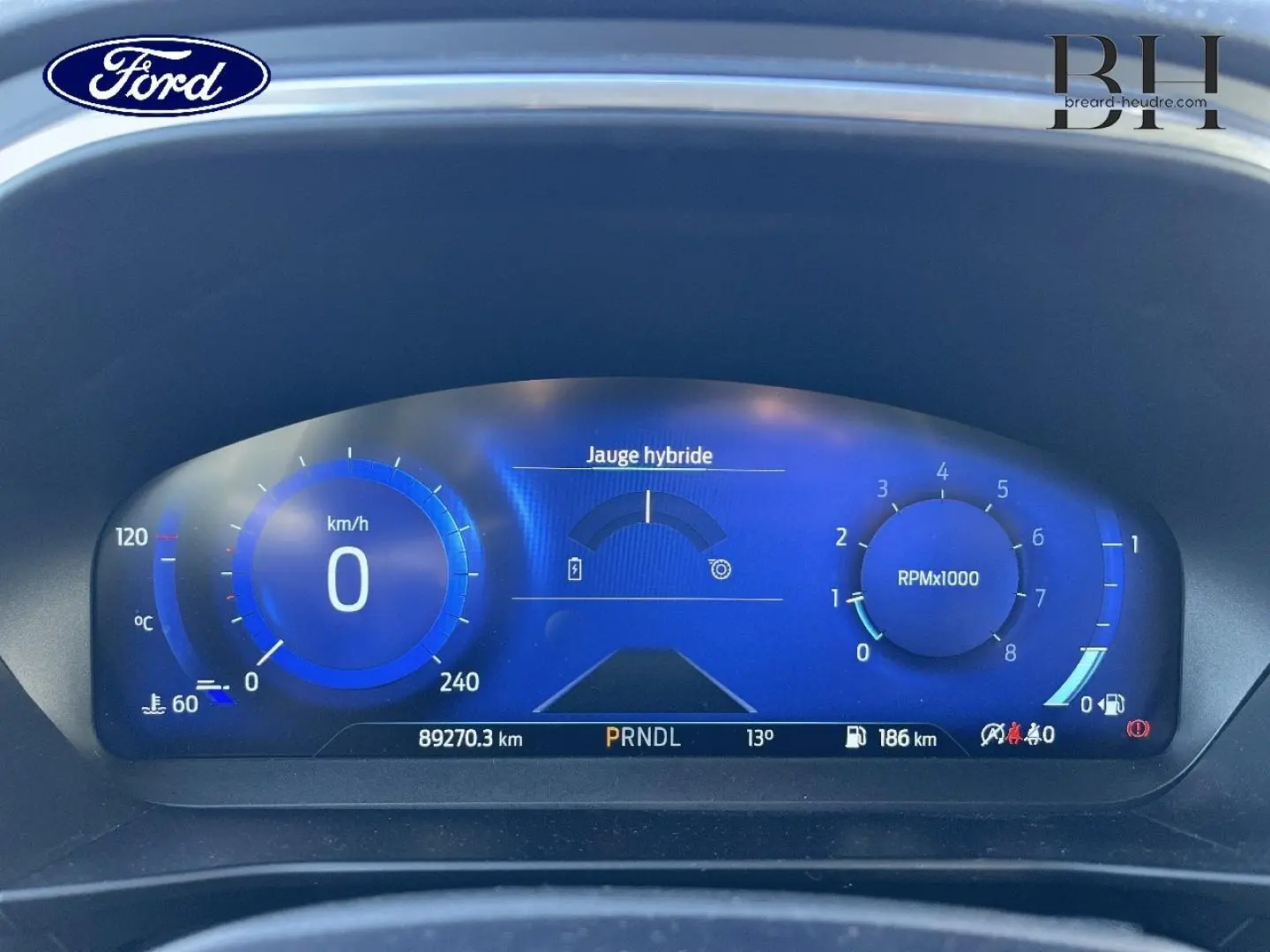 Vue rapprochée du tableau de bord numérique bleu de la Ford Focus Titanium X 2022, affichant jauge hybride et compte-tours.