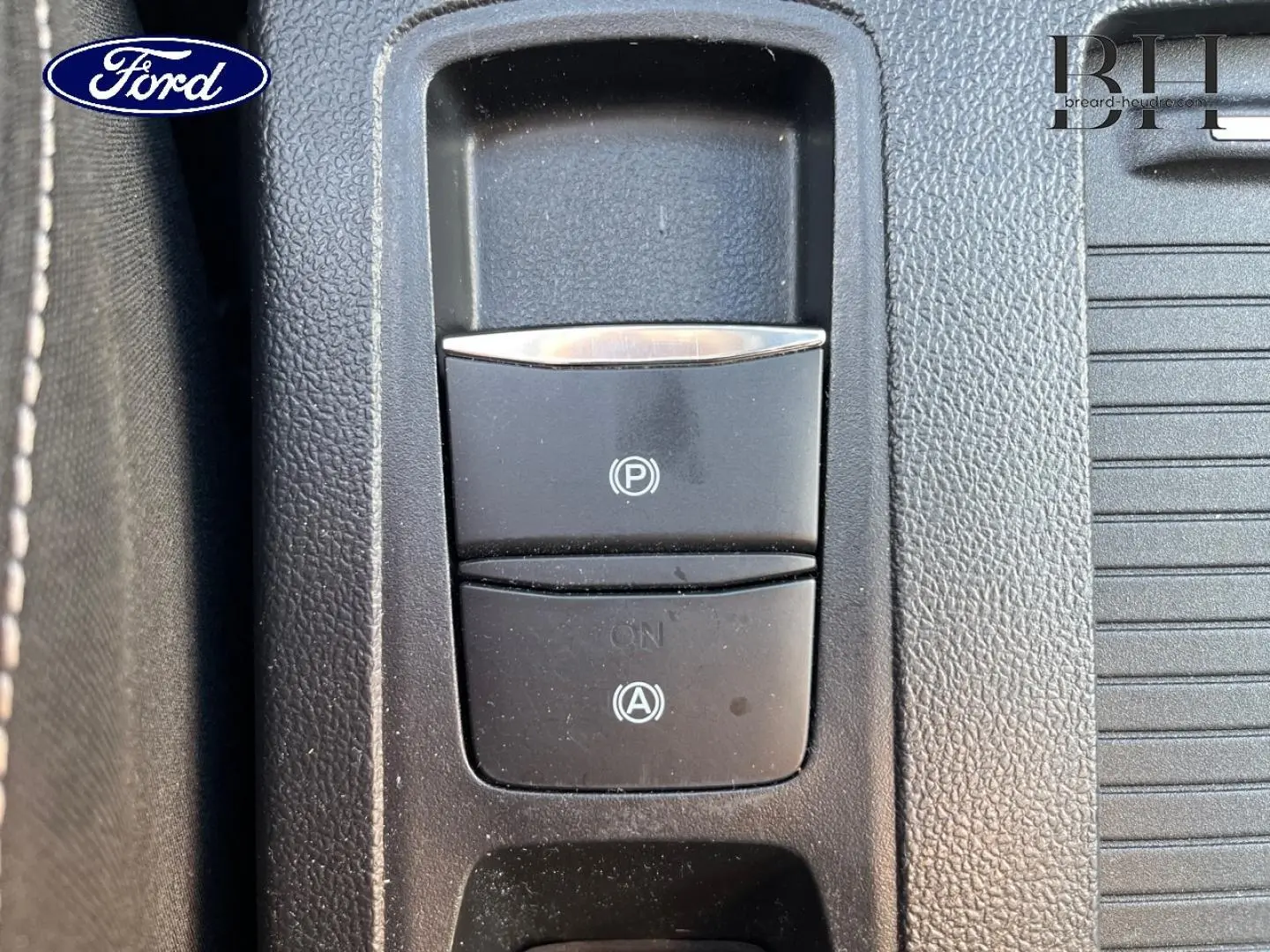 Gros plan sur les commandes de frein à main électronique et d'aide au démarrage en côte dans la console centrale noire d'une Ford Focus.