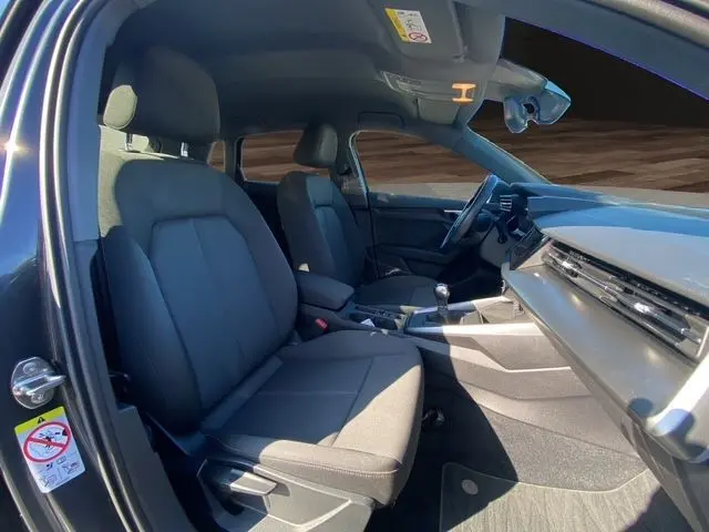 Vue intérieure côté conducteur de l'Audi A3 Sportback gris Manhattan, sièges noirs en tissu et tableau de bord moderne.