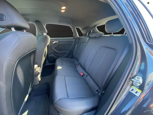 Vue intérieure arrière droit de l'Audi A3 Sportback gris Manhattan, montrant les sièges arrière en cuir noir et les portières ouvertes.