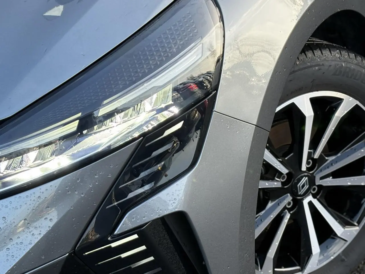 Gros plan sur le phare avant gauche et la jante alliage diamantée noire et argentée d'une Renault Clio Gris Schiste.