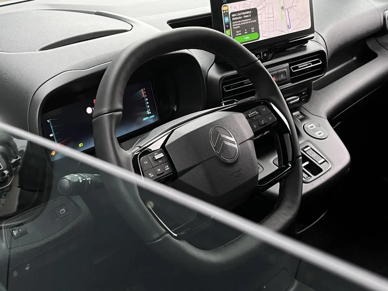 Vue intérieure du poste de conduite du Citroën Berlingo Multispace 2025, volant cuir multifonctions et écran tactile visible.