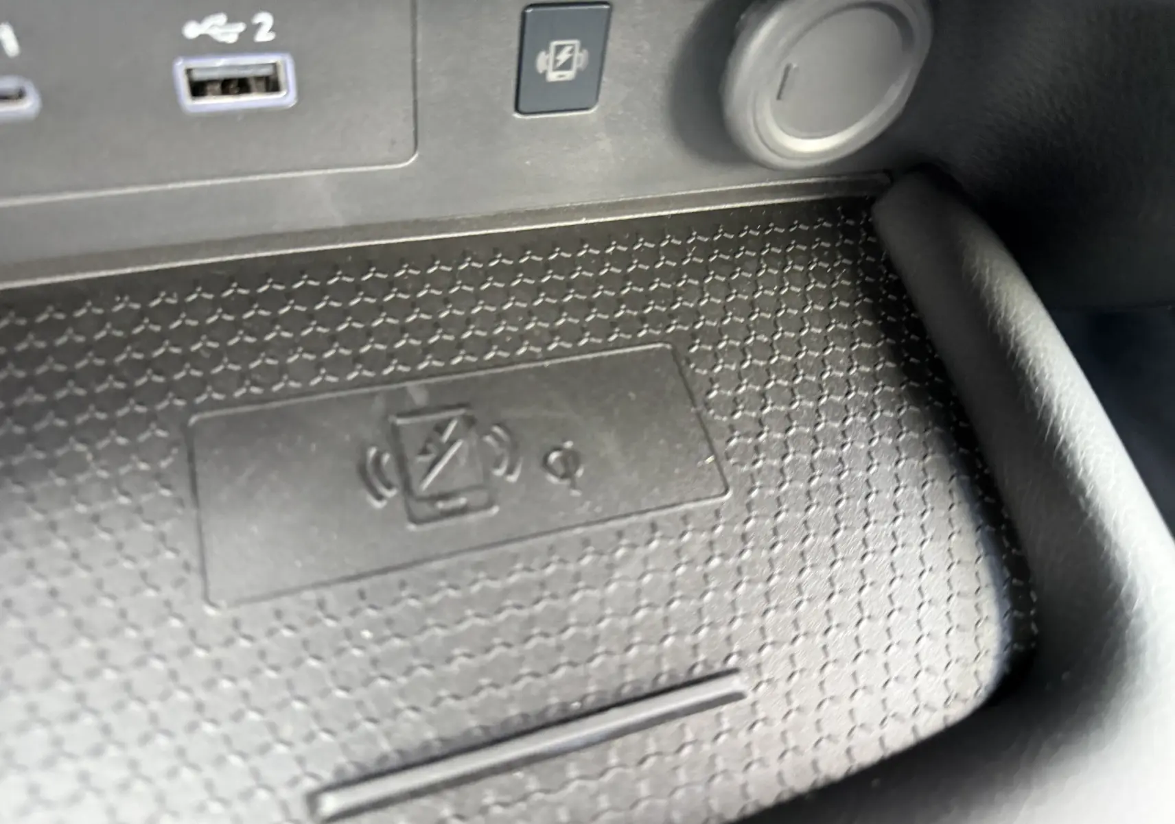 Gros plan sur la console centrale noire du Nissan Juke 1.6 Hybrid 2025, montrant la zone de recharge sans fil et ports USB.