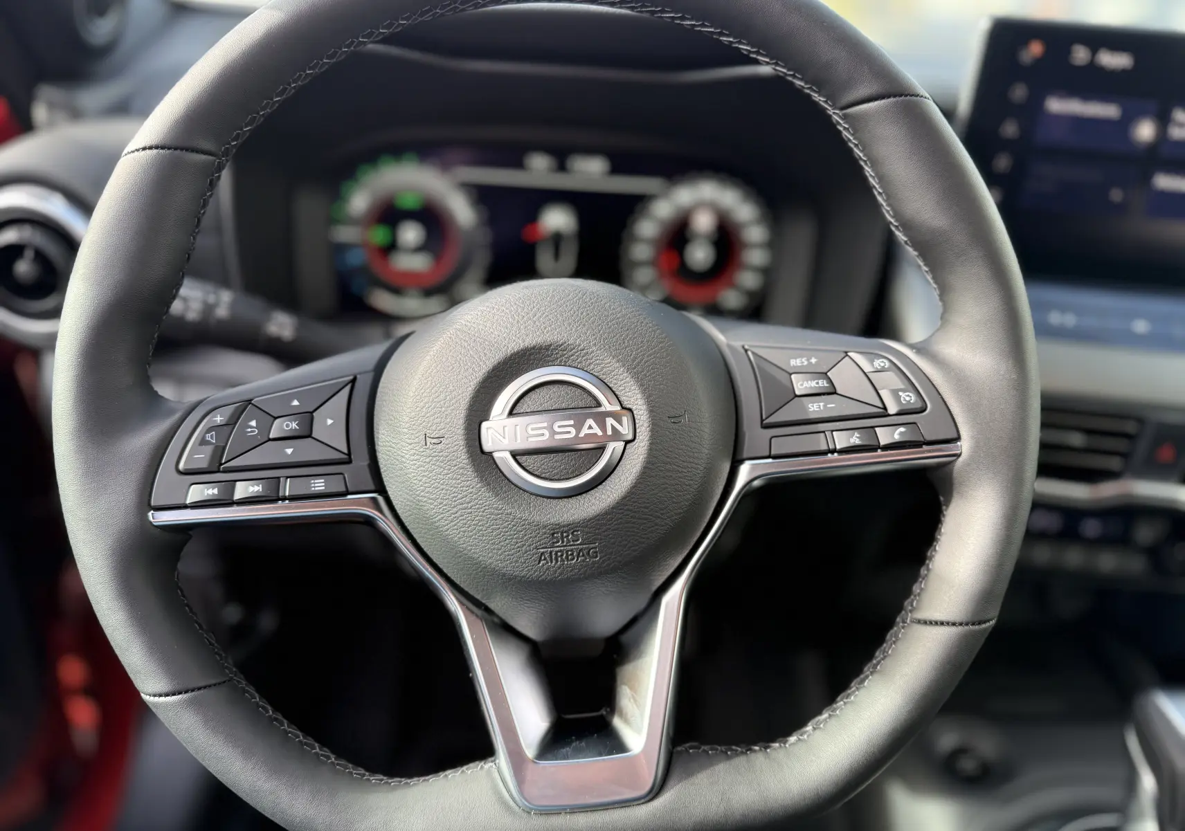 Volant en cuir noir de Nissan Juke 2025, avec commandes intégrées et tableau de bord numérique flou en arrière-plan.