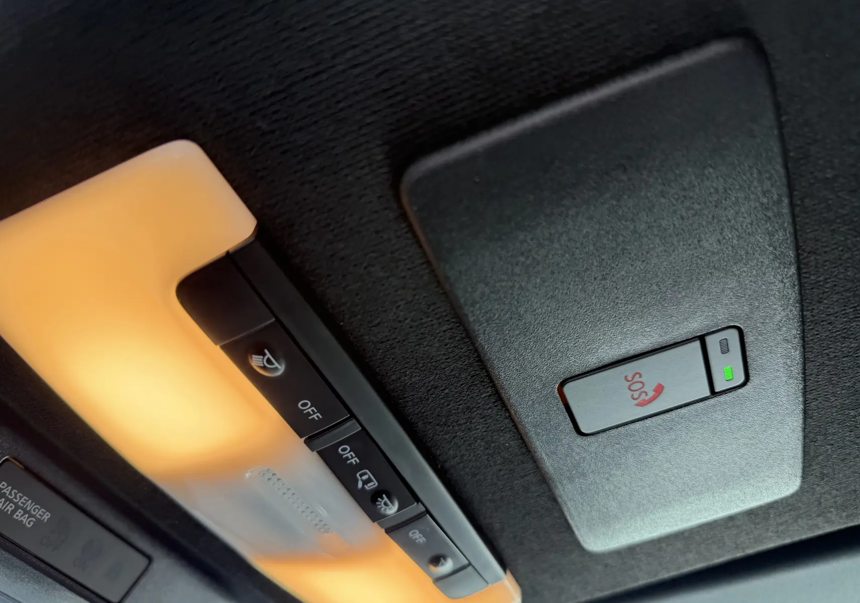 Gros plan sur la console de plafonnier intérieur avec éclairage orange et bouton SOS du Nissan Juke rouge Fuji 2025.