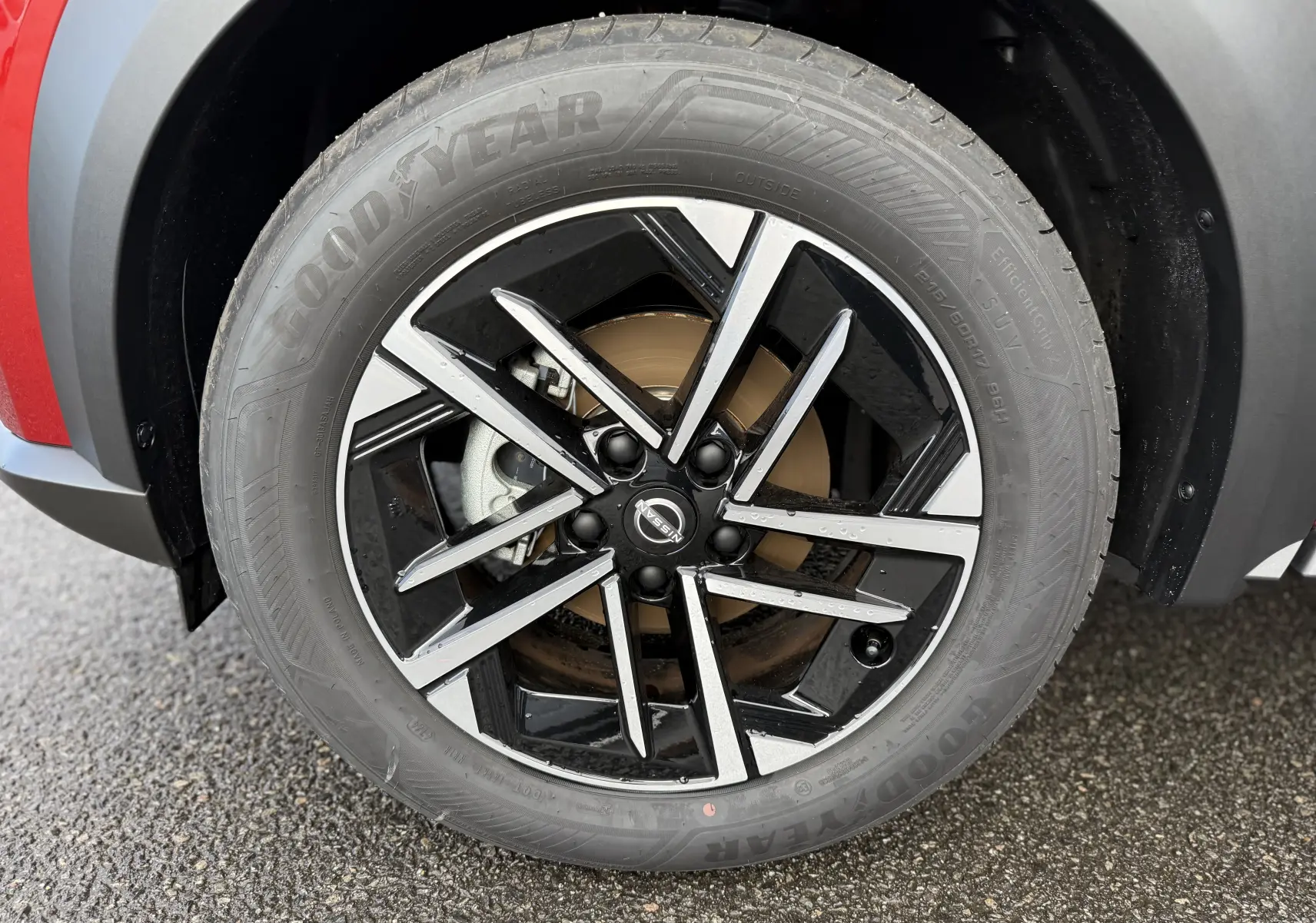 Gros plan sur la roue avant gauche du Nissan Juke rouge Fuji, mettant en valeur la jante noire et argentée au design moderne.