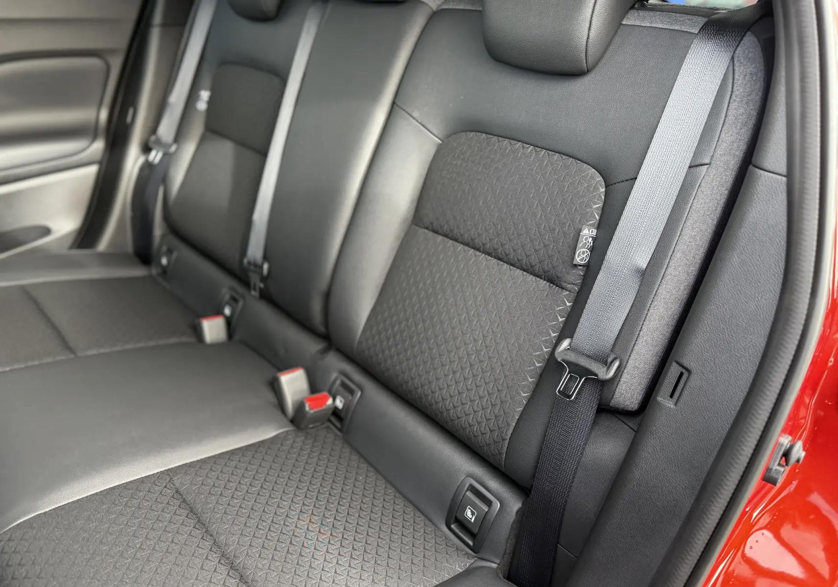 Vue rapprochée des sièges arrière noirs avec ceinture grise du Nissan Juke rouge Fuji, version hybride 2025.