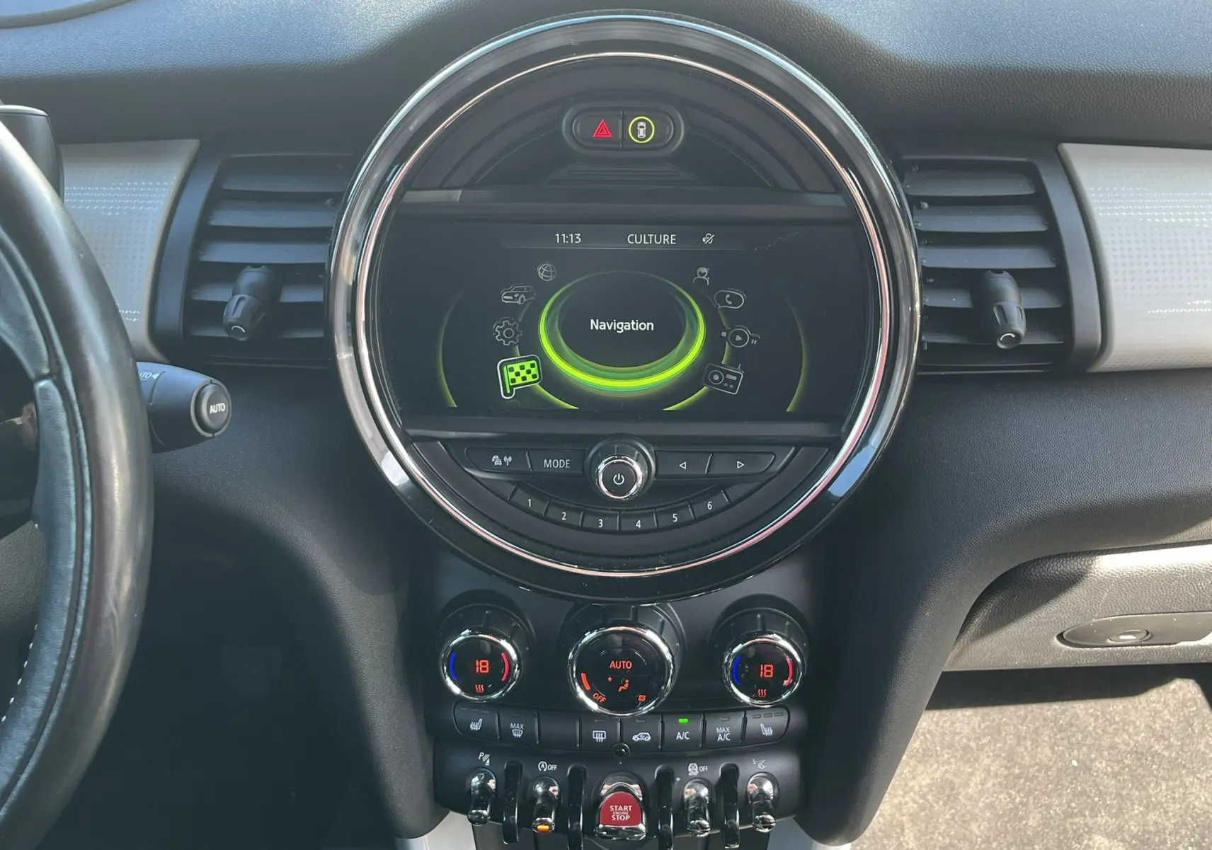 Vue rapprochée du tableau de bord central de la MINI Cabriolet bleu, avec écran de navigation circulaire et commandes climatisation.