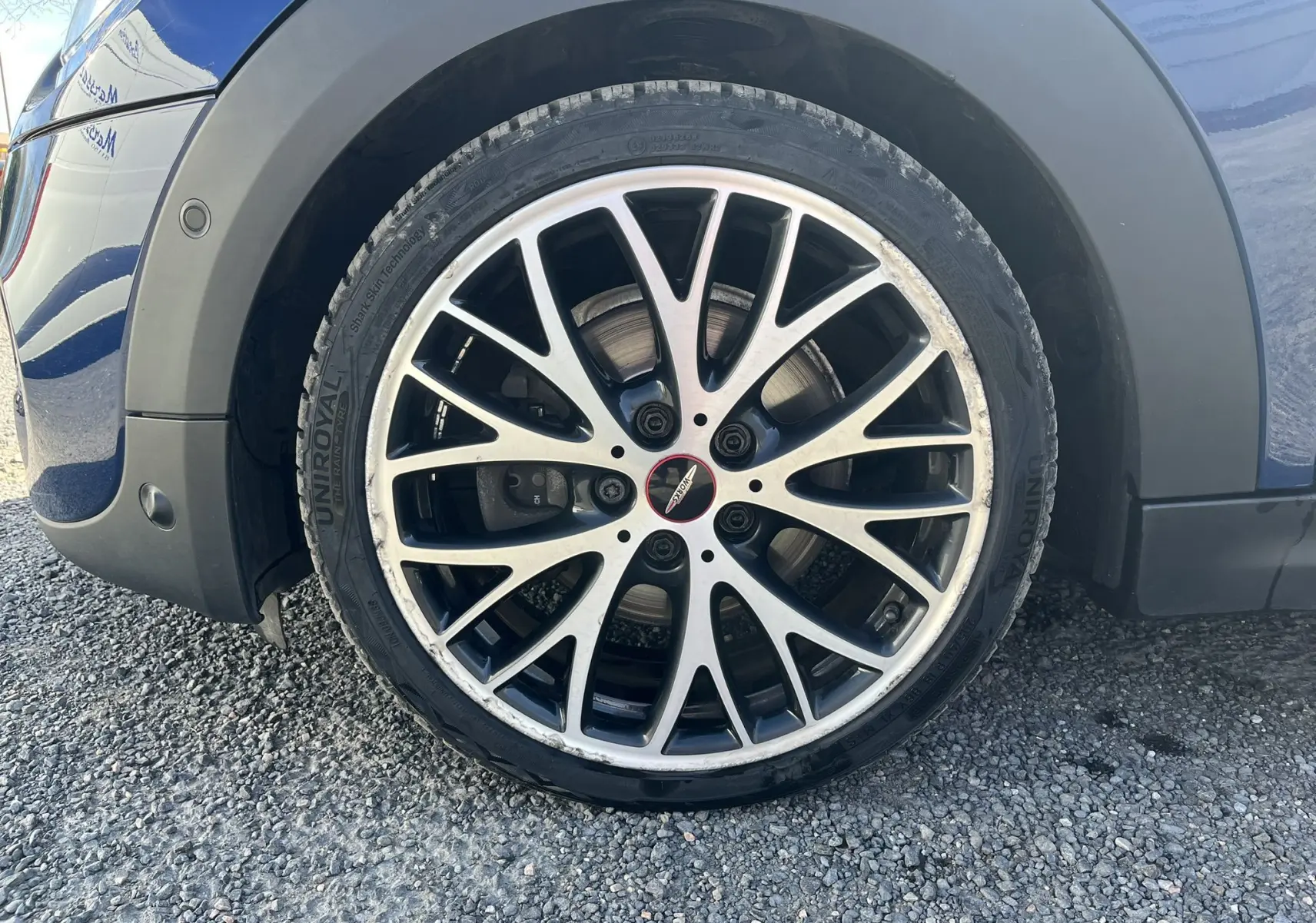Gros plan sur la jante avant droite bicolore du MINI Cabriolet bleu, avec logo John Cooper Works au centre.