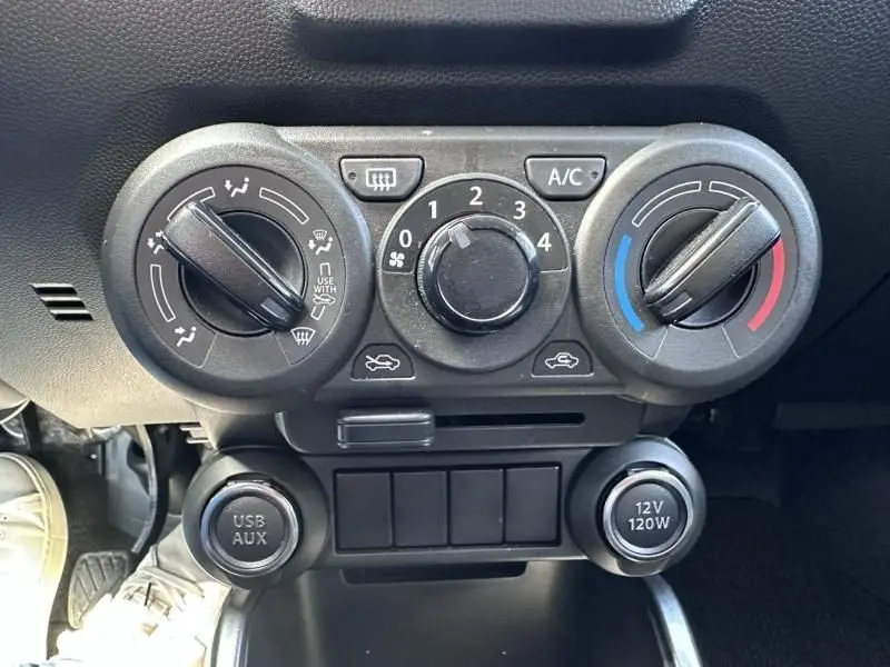 Vue rapprochée des commandes manuelles de climatisation et ventilation du Suzuki Ignis beige 2023, avec boutons rotatifs et prises USB/AUX et 12V.