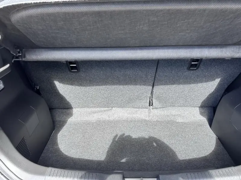 Coffre ouvert vu de l'arrière d'une Suzuki Ignis beige 2023, montrant l'espace de chargement vide et la moquette grise.