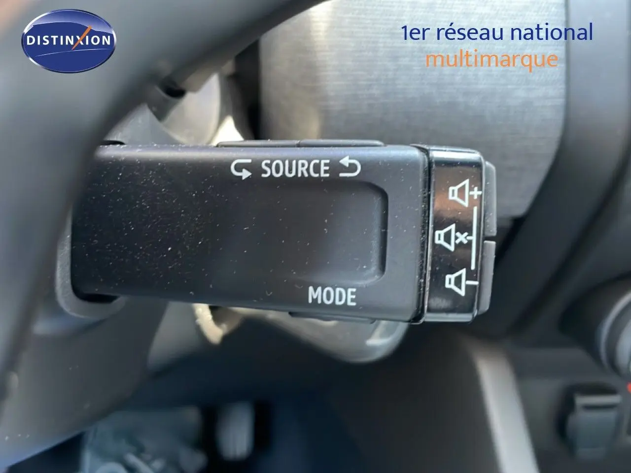 Gros plan sur la commande au volant de la Renault Clio noire, avec boutons source et mode visibles.