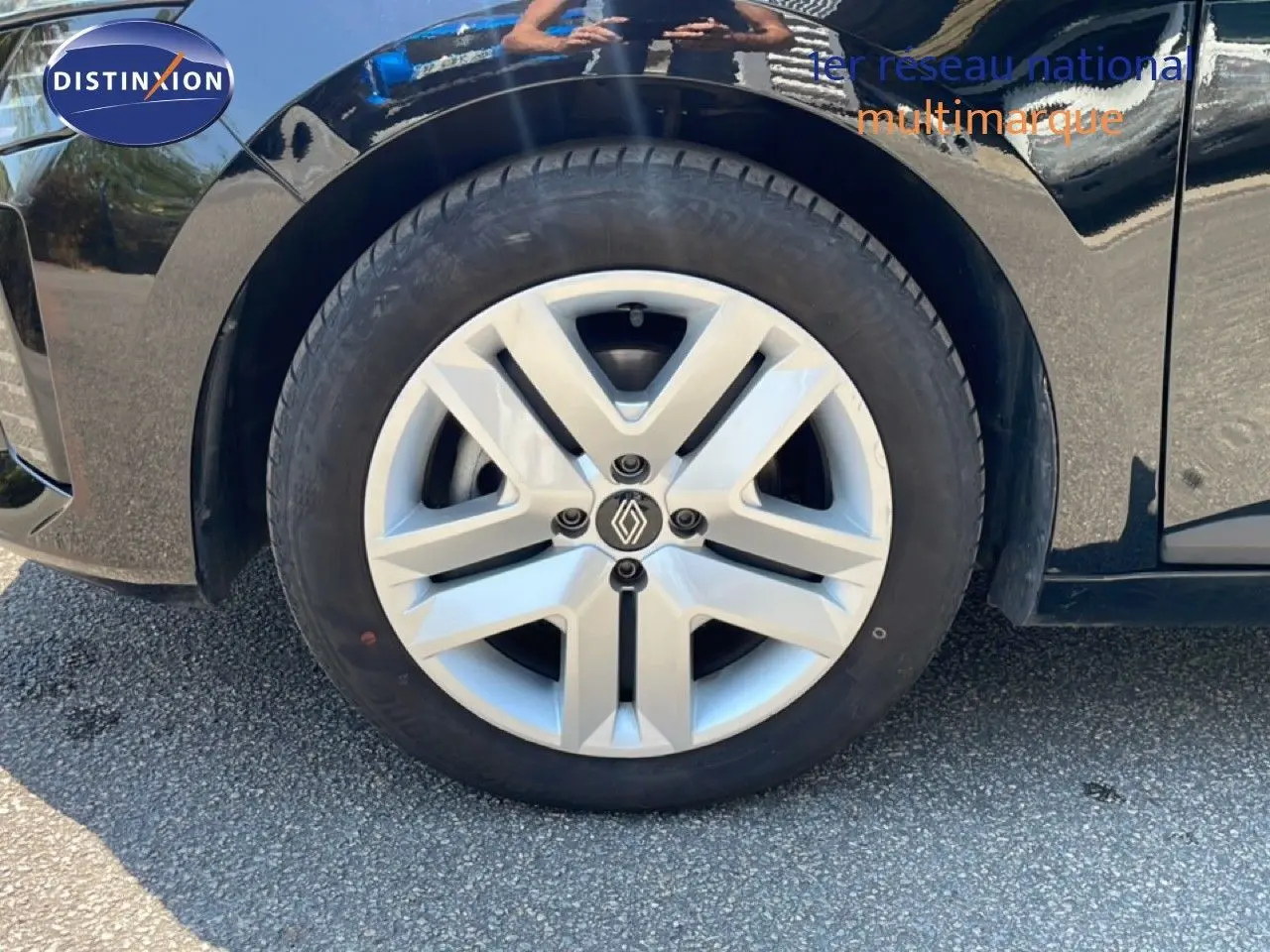 Gros plan sur la roue avant gauche d'une Renault Clio noire étoile métal, mettant en valeur la jante argentée au logo Renault.