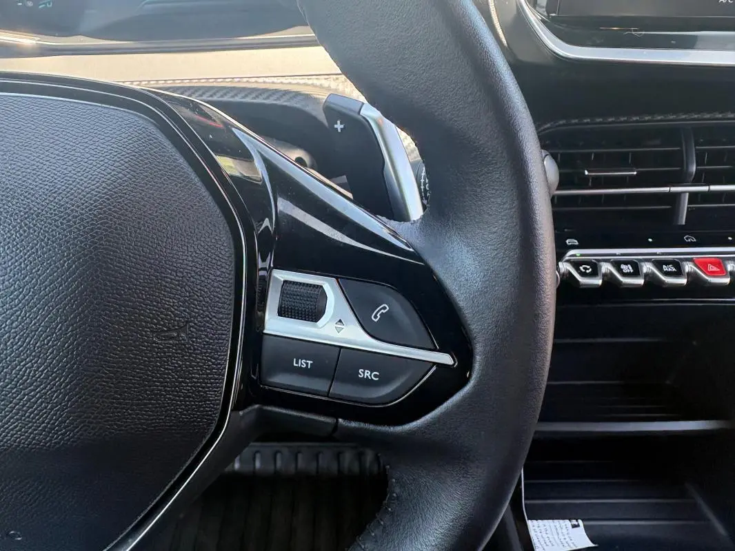Gros plan sur le volant côté gauche du Peugeot 2008 gris, avec commandes audio et tableau de bord noir.