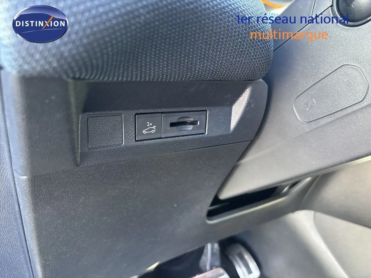 Détail intérieur montrant le bouton d'ouverture du coffre sur la partie inférieure gauche du tableau de bord noir.