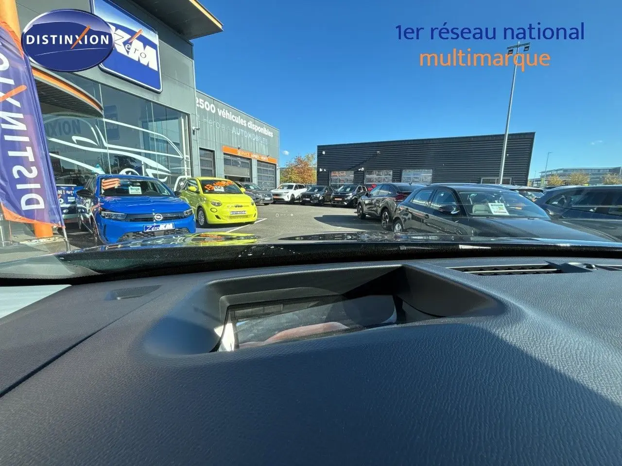 Vue depuis l'intérieur vers l'extérieur, montrant un Citroën C5 Aircross bleu Eclipse métal avec toit noir en 3/4 avant gauche.