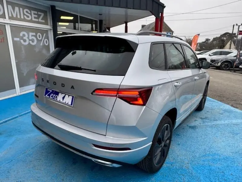 Vue 3/4 arrière droite du Skoda Karoq gris diamant métallisé avec feux arrière LED allumés sur parking.