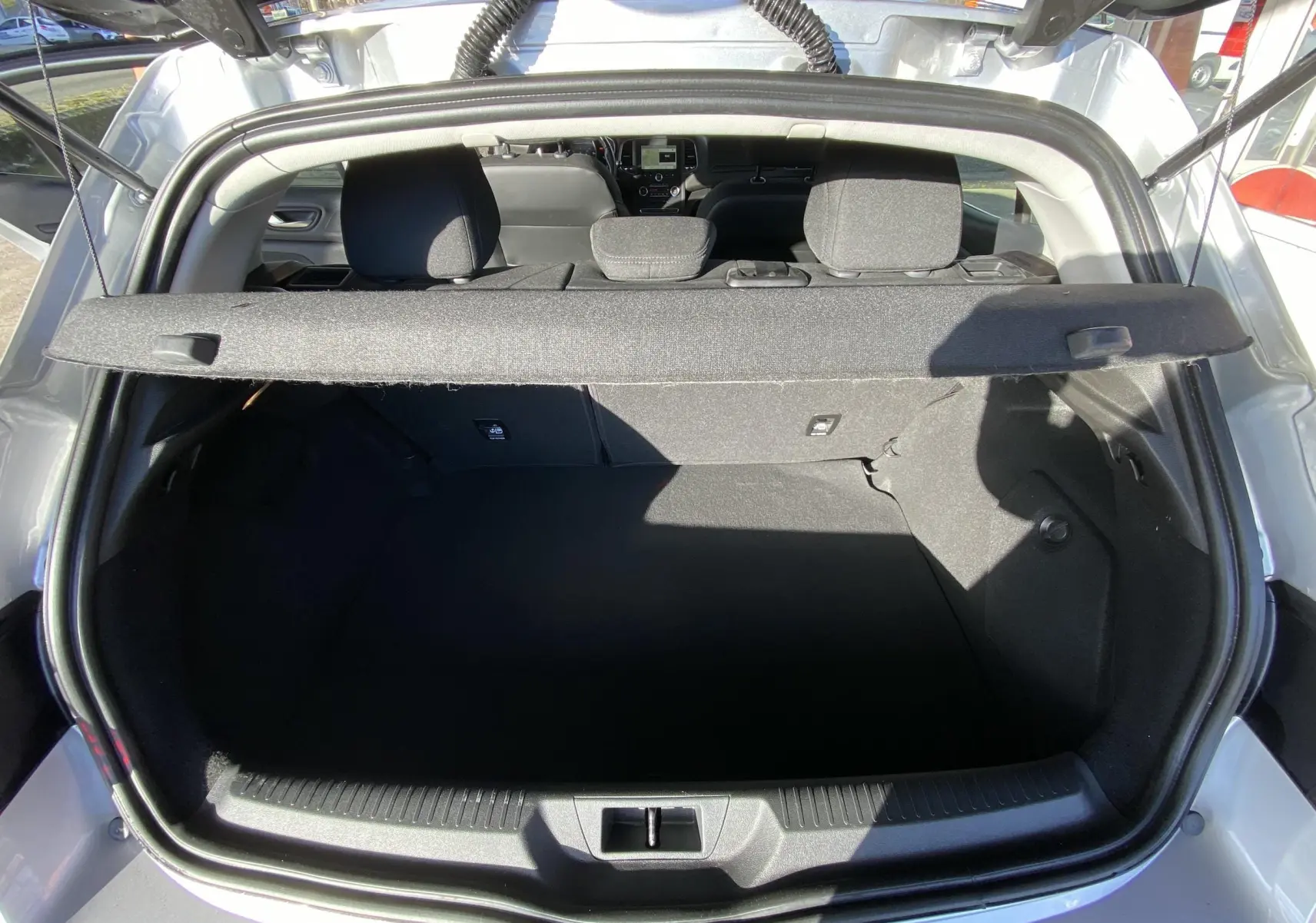 Coffre ouvert vu de l'arrière d'une Renault Mégane IV Berline gris, avec banquette arrière et tablette cache-bagages visible.