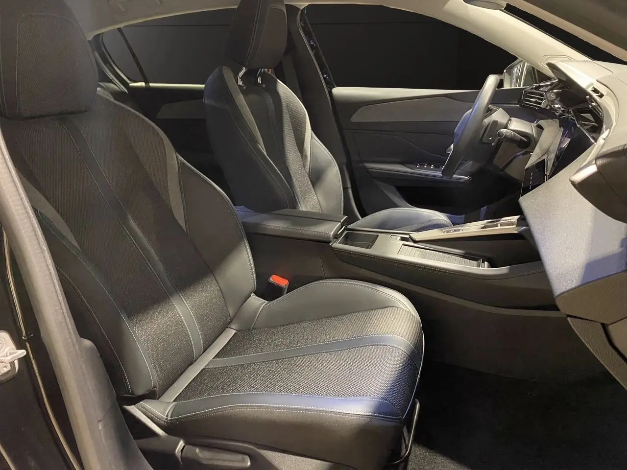 Intérieur noir de la Peugeot 308 2024, vue côté gauche sur les sièges avant en cuir et tissu avec console centrale moderne.