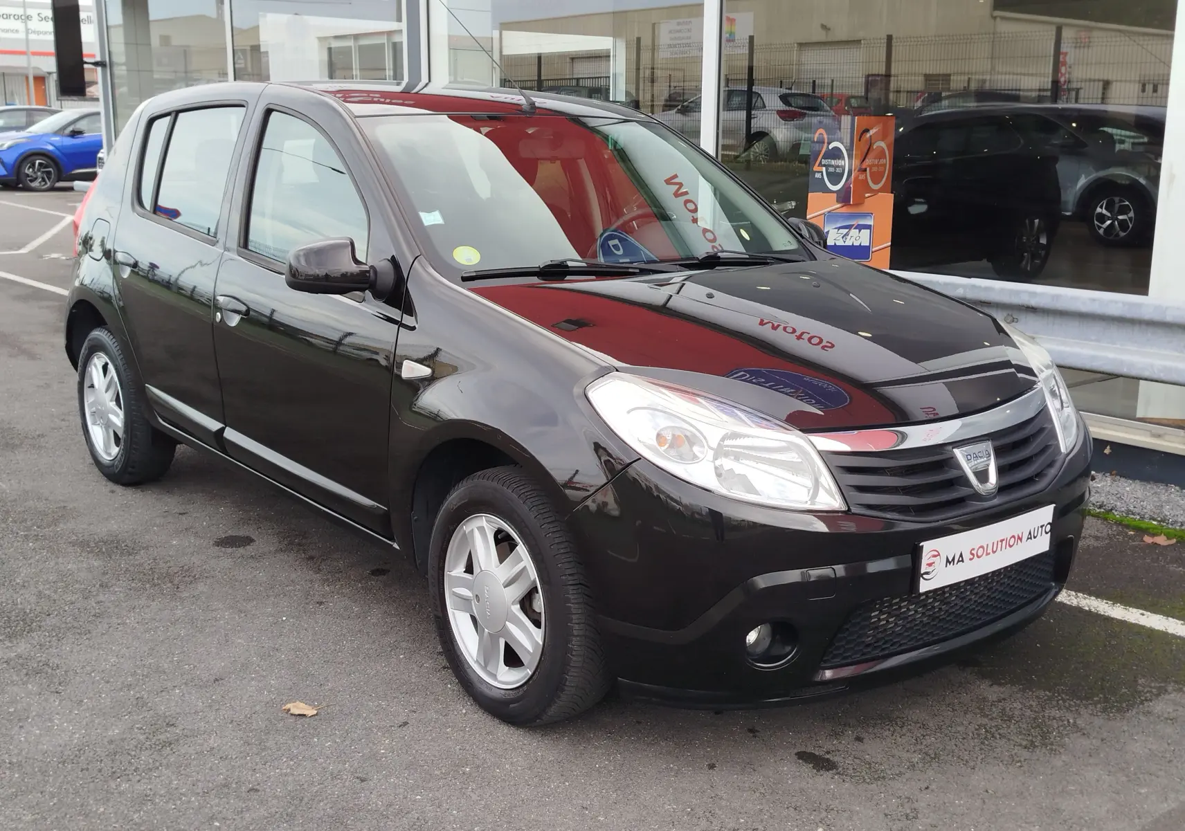 Dacia Sandero noire vue en 3/4 avant droit, avec calandre chromée et jantes alliage 15 pouces visibles.