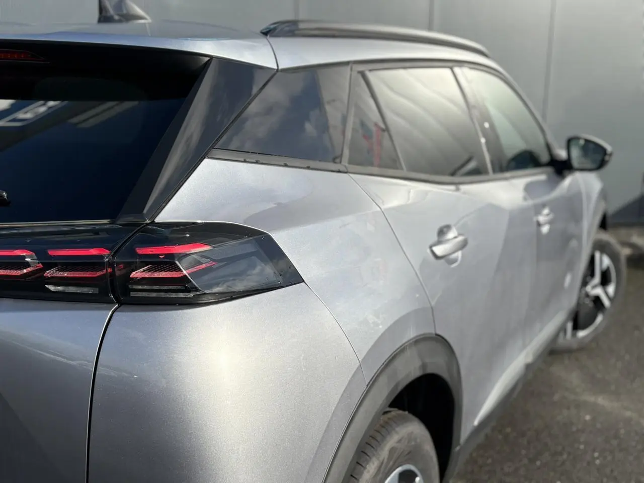 Vue 3/4 arrière droite d’un Peugeot 2008 Hybrid 145 gris Artense avec feux arrière LED à 3 griffes et jantes bi-ton.