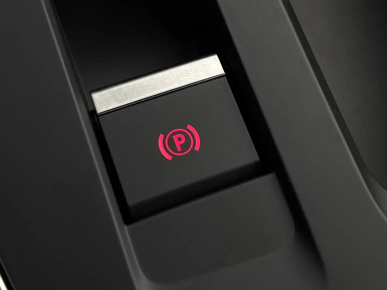 Gros plan sur le bouton de frein de stationnement électrique illuminé en rouge dans le coffre central du Citroën C5 Aircross.