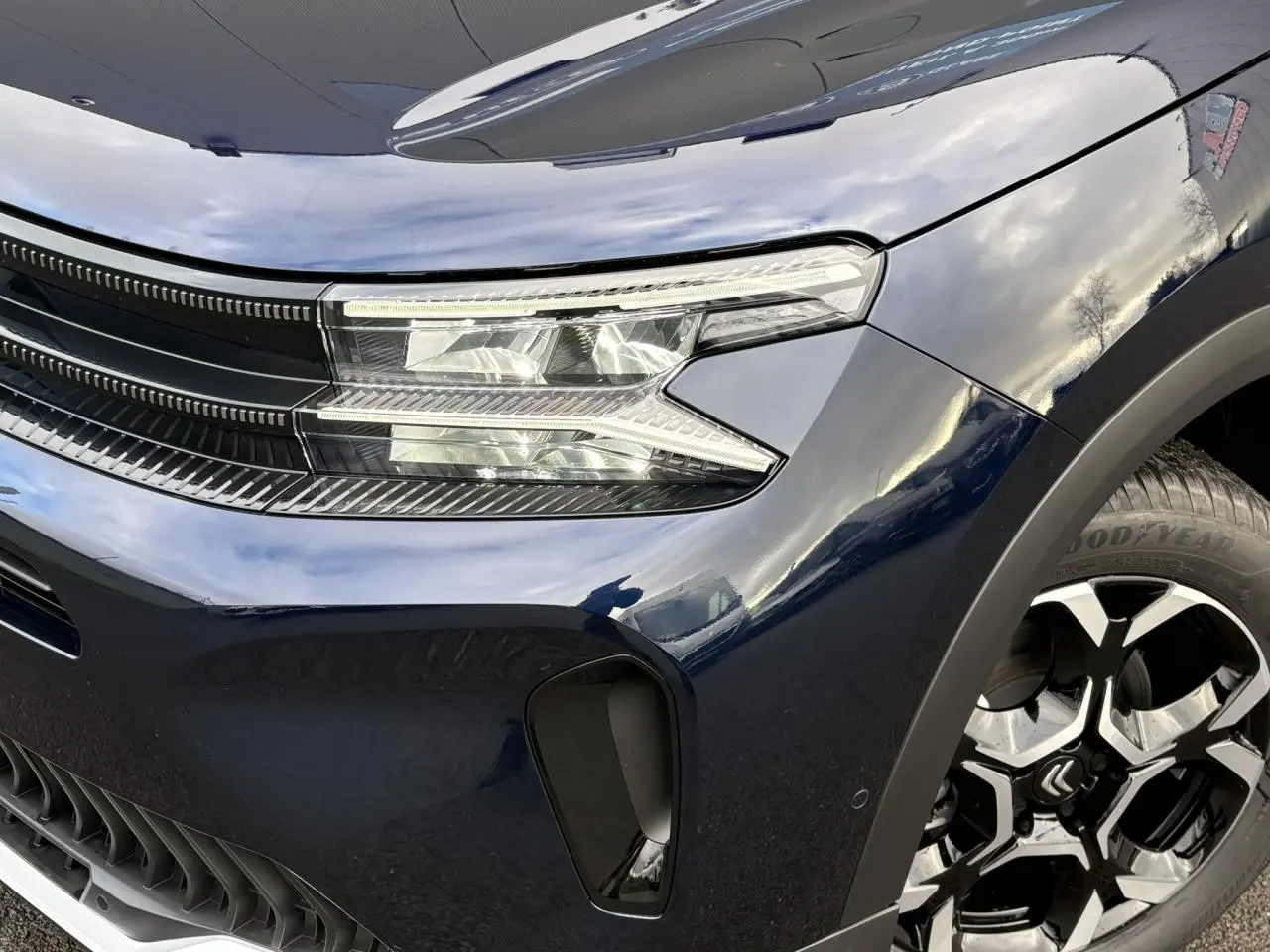 Gros plan sur l'avant droit bleu Eclipse du Citroën C5 Aircross 2025, mettant en valeur le phare LED et la jante alliage bi-ton.