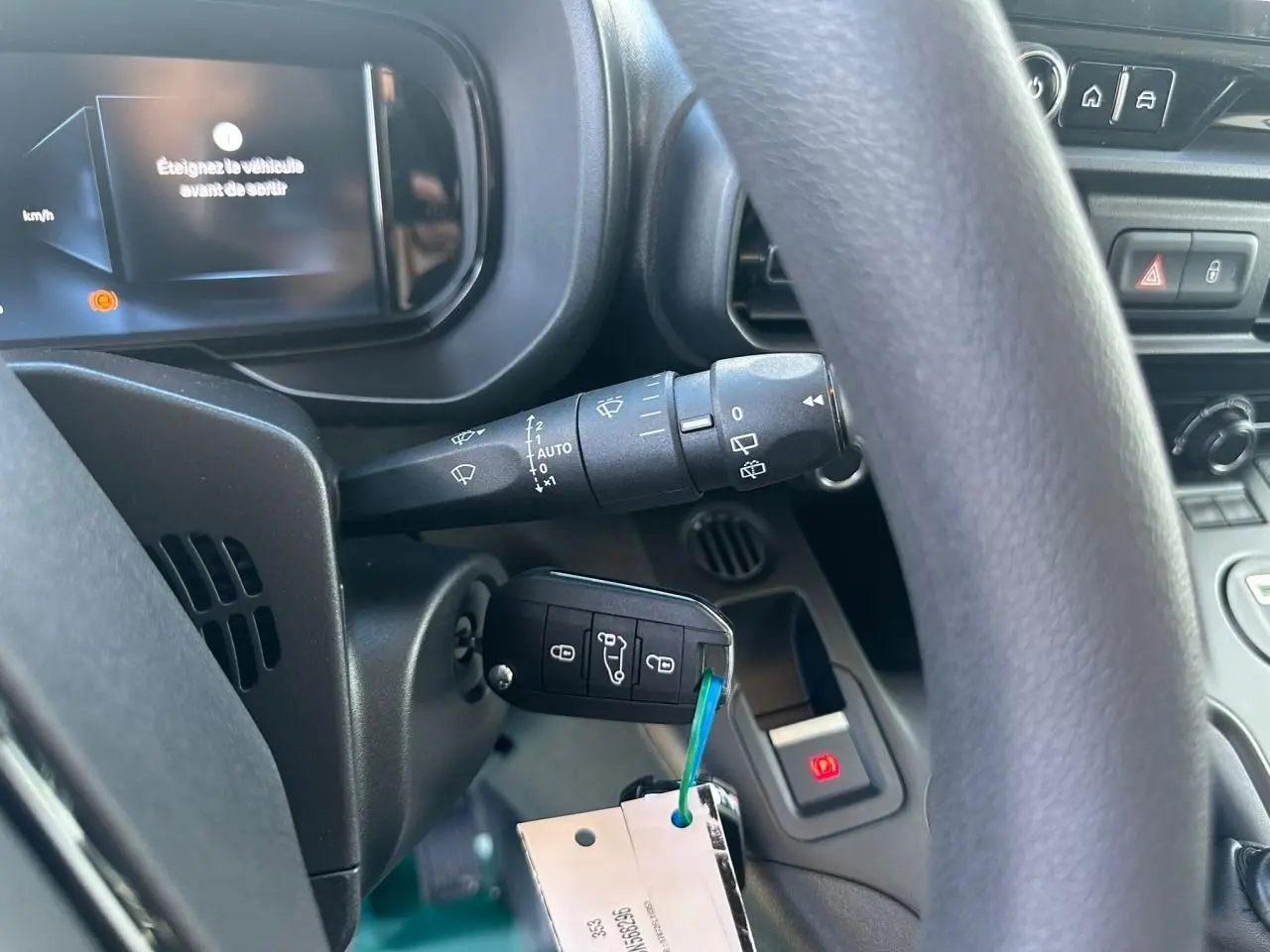 Gros plan intérieur sur le volant et le tableau de bord du Citroën Berlingo blanc, avec clé insérée et écran numérique allumé.