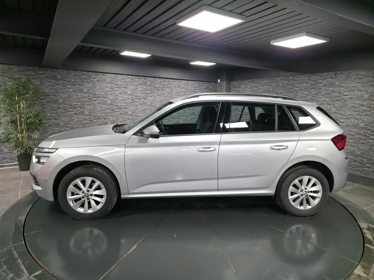 Vue latérale droite d’un Skoda Kamiq gris métallisé 2023, avec jantes alliage 16 pouces et barres de toit noires.