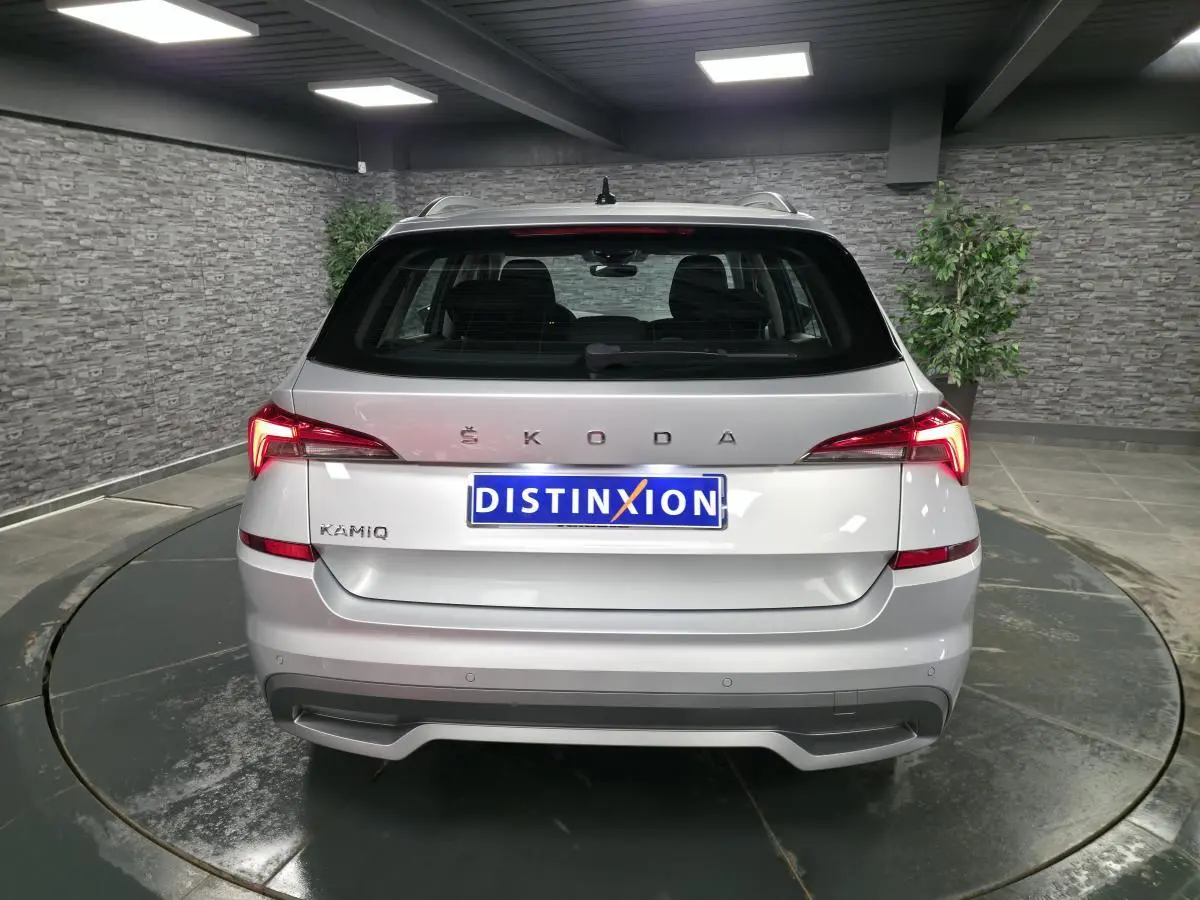 Vue arrière d'un Skoda Kamiq gris métallisé 2023 avec feux arrière LED et logo ŠKODA visible sur un plateau tournant intérieur.