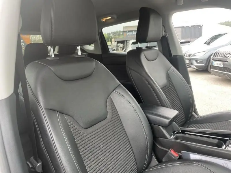 Vue intérieure sur les sièges avant en cuir noir du Jeep Compass blanc 2023, avec accoudoir central et ceinture de sécurité visible.