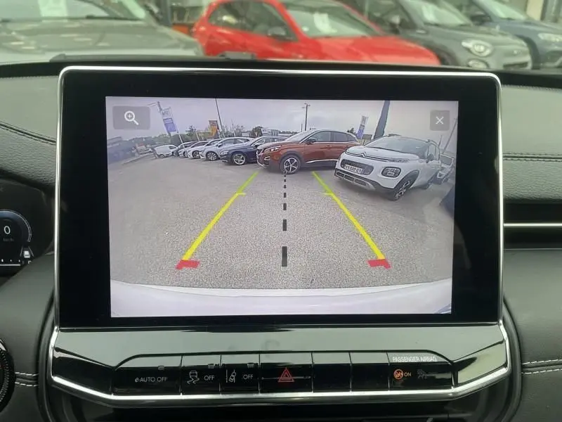 Vue arrière via caméra de recul du Jeep Compass blanc 2023, avec lignes de guidage jaunes et rouges visibles à l'écran.