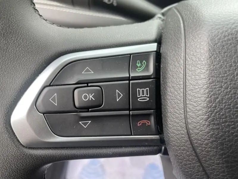 Gros plan sur les commandes au volant côté gauche du Jeep Compass blanc 2023, boutons de navigation et appel téléphonique.