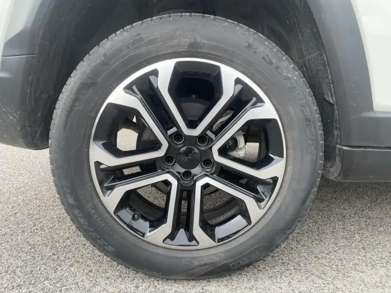 Gros plan sur la roue avant droite d’un Jeep Compass blanc 2023, mettant en valeur la jante en alliage noir et argent.