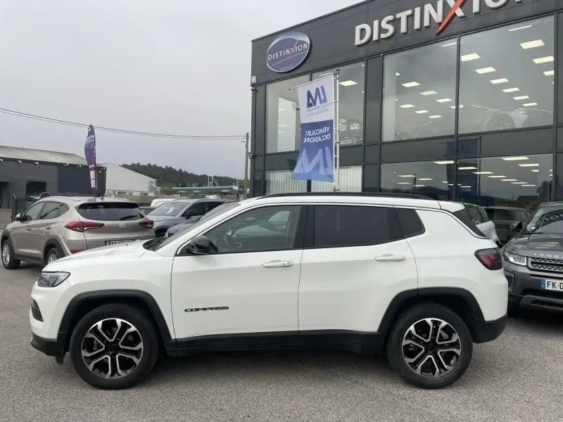 Vue de profil côté gauche d'un Jeep Compass blanc 2023 avec jantes noires et détails noirs contrastants, stationné devant un showroom.