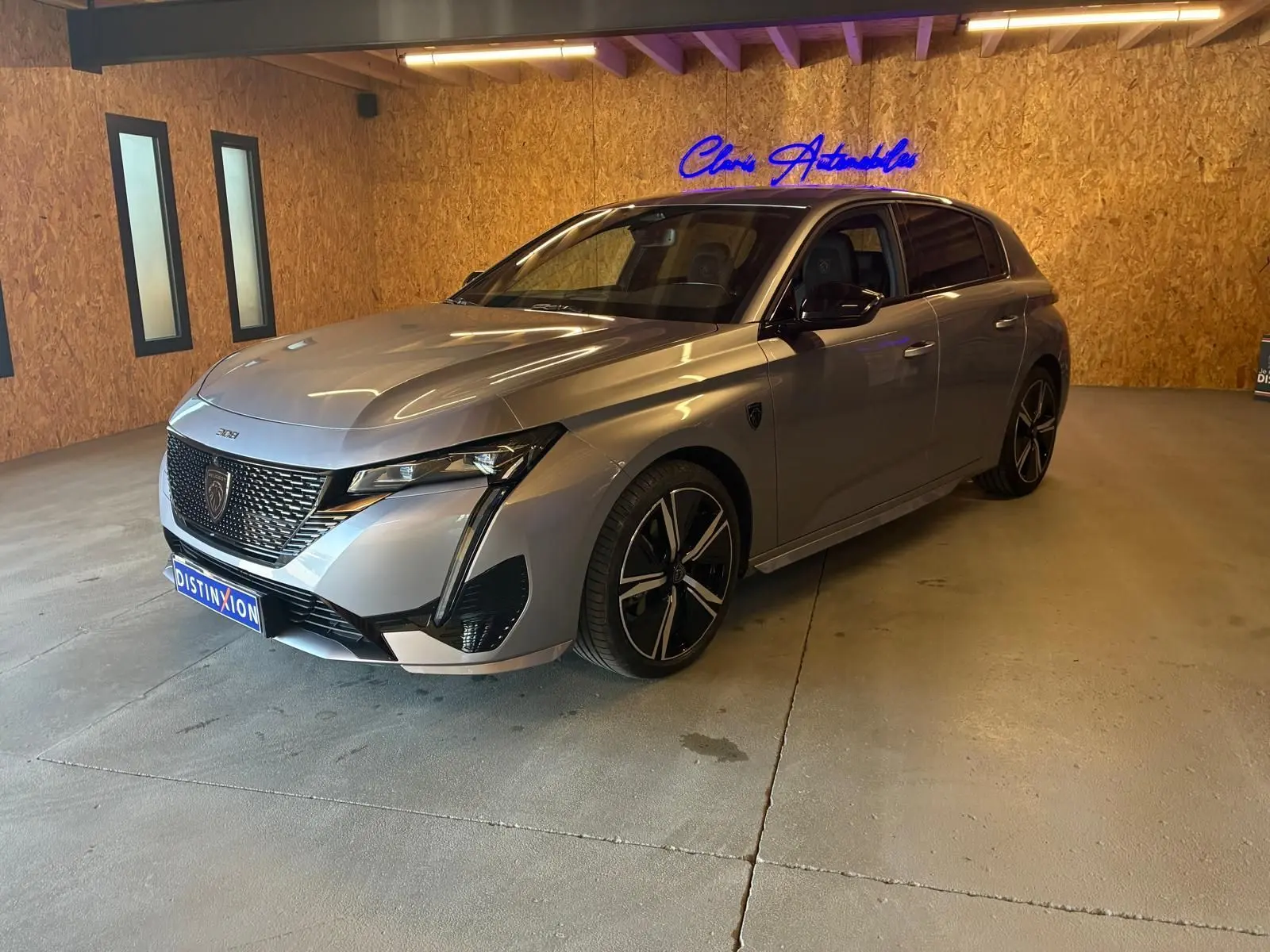 Peugeot 308 gris vue 3/4 avant droit en intérieur, avec calandre distinctive et jantes noires bicolores.