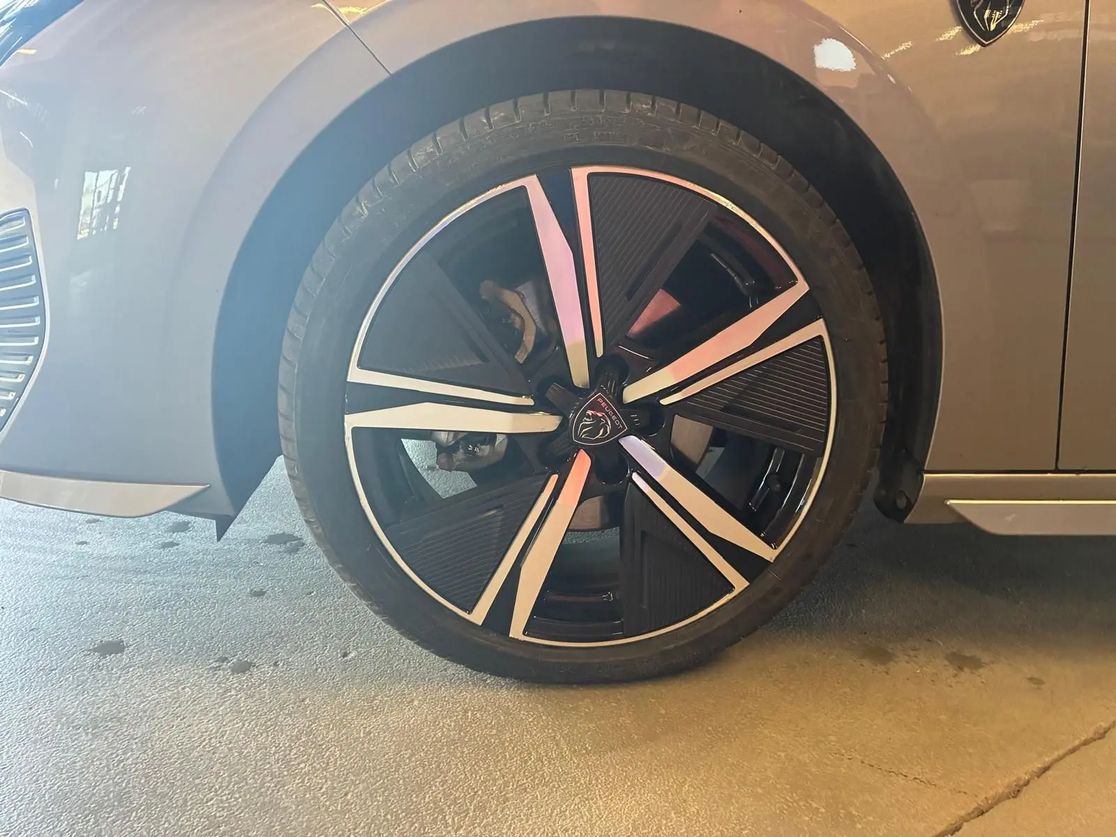 Gros plan sur la roue avant gauche d’une Peugeot 308 gris 2025, jante noire et argent avec logo lion au centre.