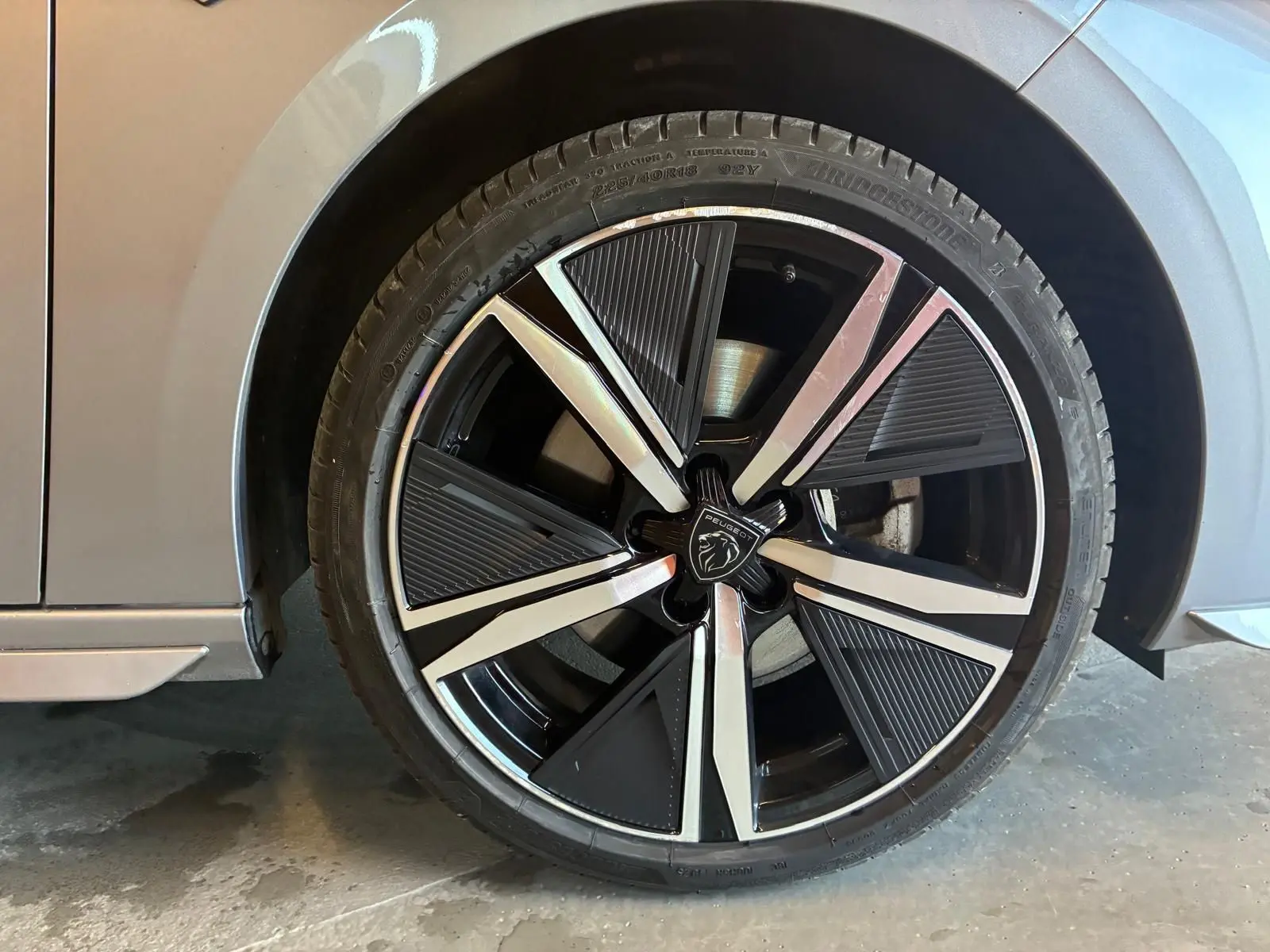 Gros plan sur la roue avant droite grise d'une Peugeot 308 1.2 Hybrid 136 E-DCS6 GT avec jante noire et argentée.