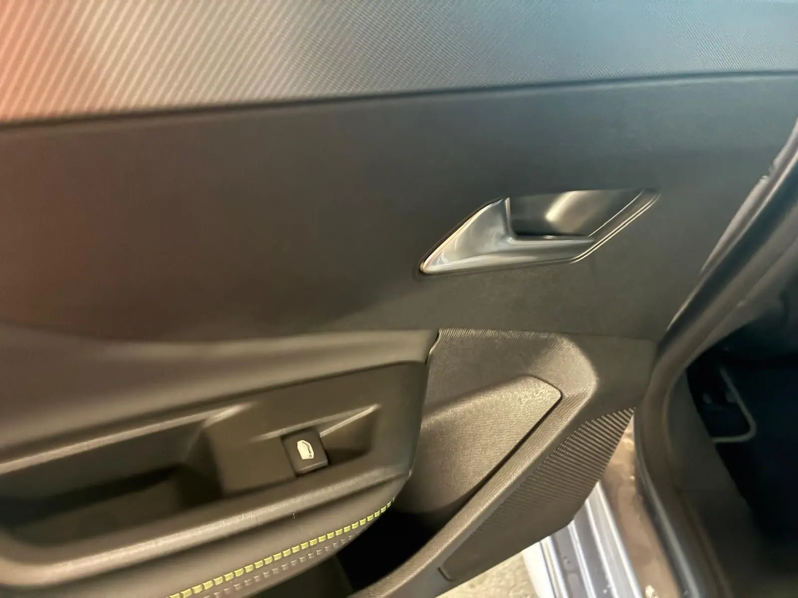 Détail de la porte intérieure côté gauche d'une Peugeot 308 gris, montrant la poignée et le bouton de verrouillage.