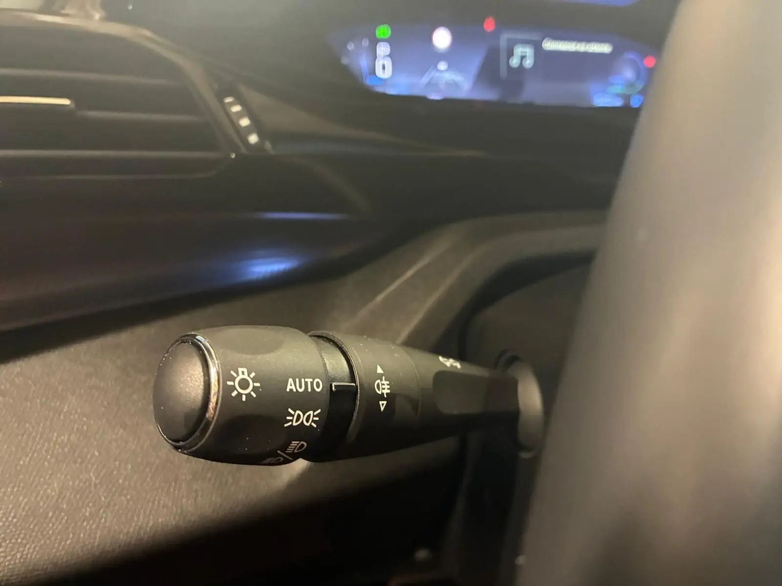 Gros plan sur la commande d’éclairage à gauche du volant dans l’habitacle noir de la Peugeot 308 gris 1.2 Hybrid 136 E-DCS6 GT 2025.