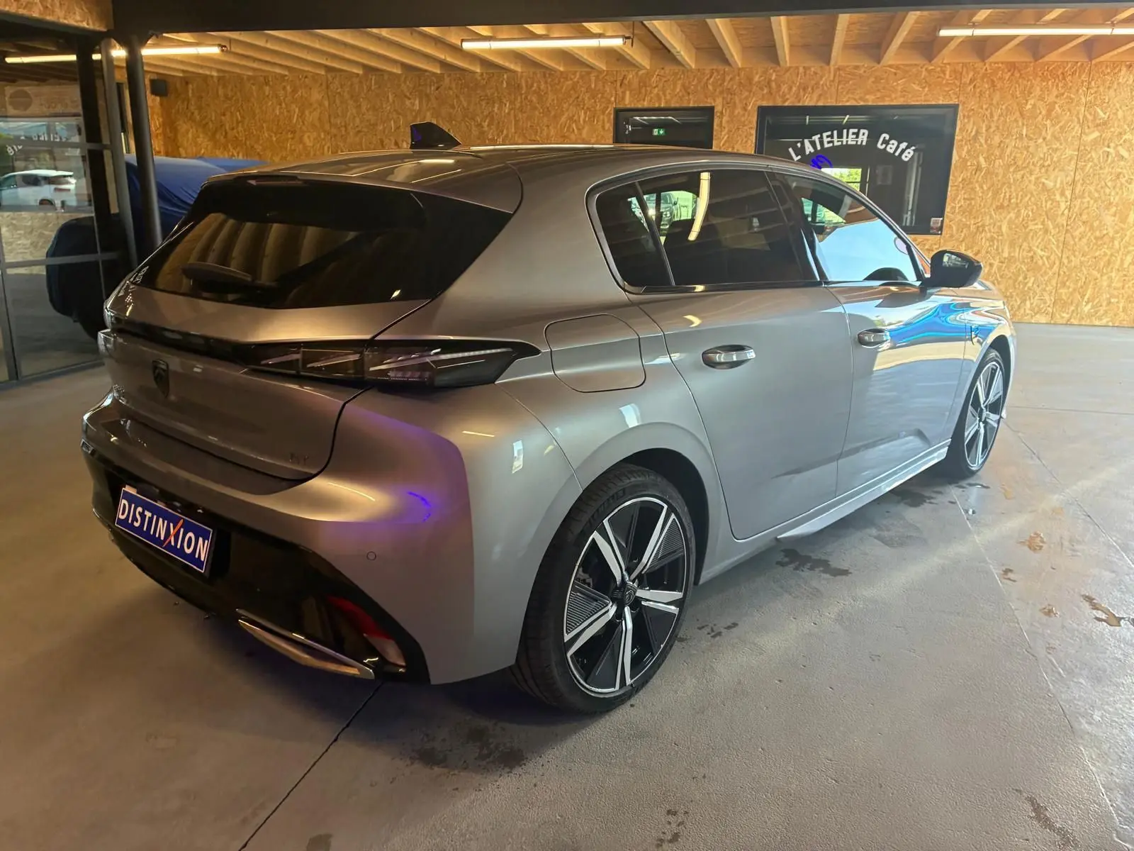 Vue 3/4 arrière droite d'une Peugeot 308 gris métallisé avec jantes alliage et feux arrière LED, stationnée en intérieur.